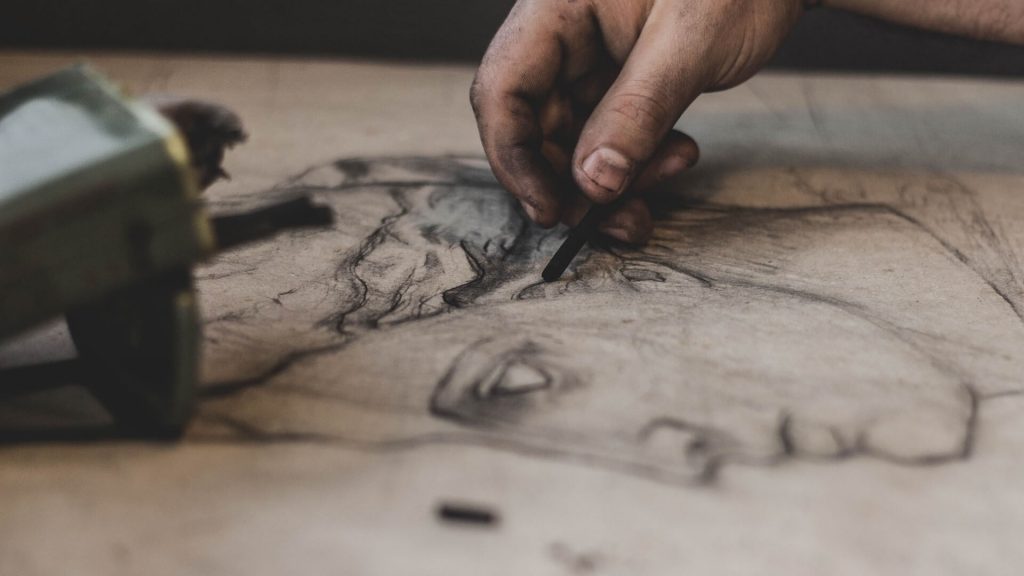 Una persona utilizando carboncillo para crear un dibujo, capturando el proceso artístico en acción.